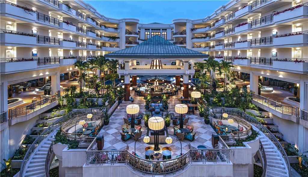 Luxurious hotel atrium with multi-storey balconies, a central lounge, and lush palms.