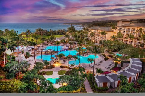A tropical resort at sunset with multiple swimming pools, palm trees, and a beachfront hotel.