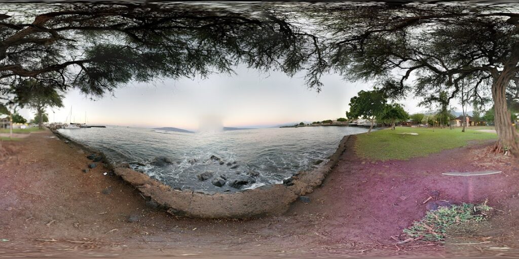 Panoramic view of a lakeside park with a rocky breakwater, calm water, and trees framing the scene on both sides.