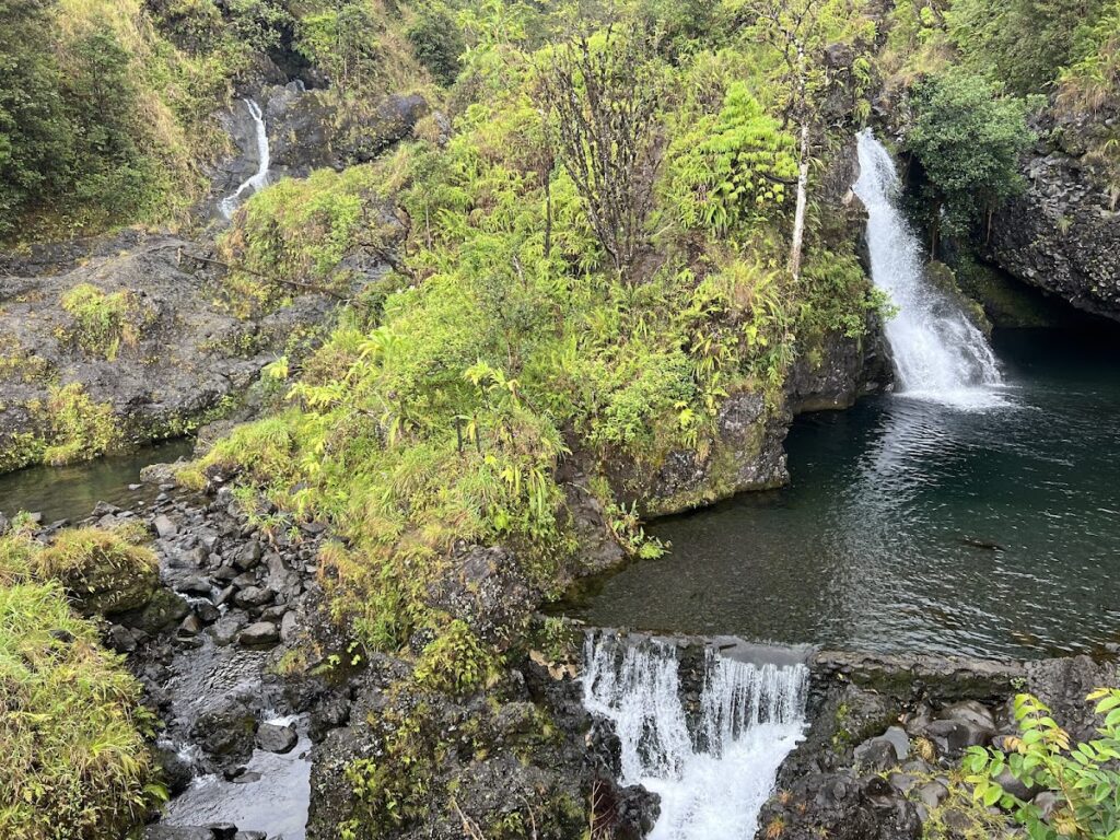 Brush Fire Near Olinda Road Contained Same Day - Maui Tom's Vacation Rental Cleaning & Maintenance Lush rocky gorge with multiple small waterfalls feeding a dark pool amid green foliage.