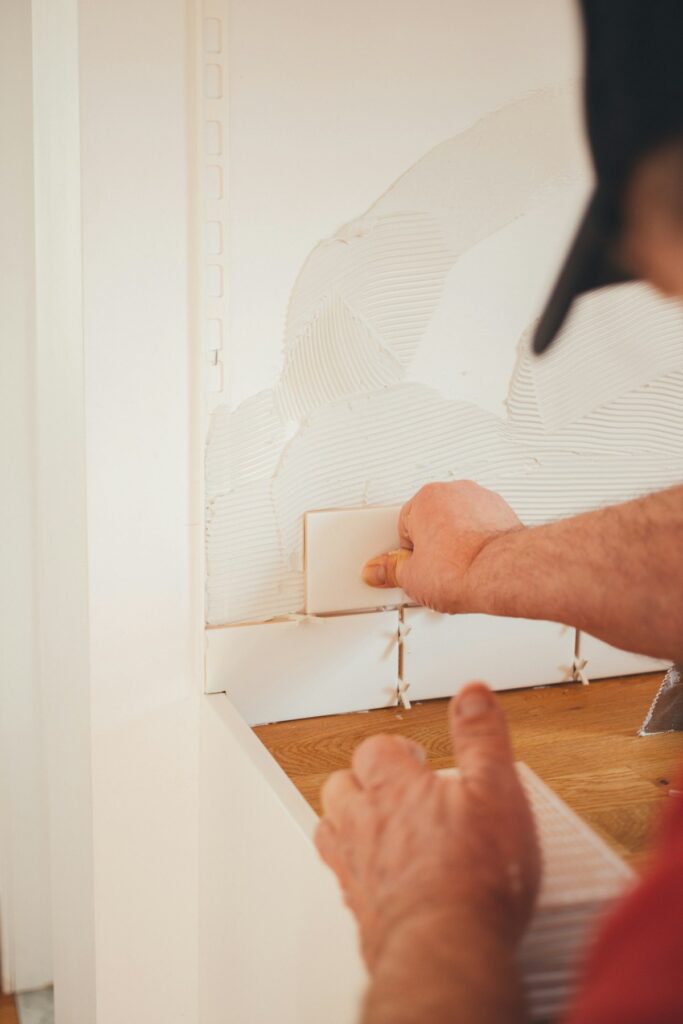 Close-up of a person’s hands pressing a white tile into place on a wall with adhesive, part of a tiling job