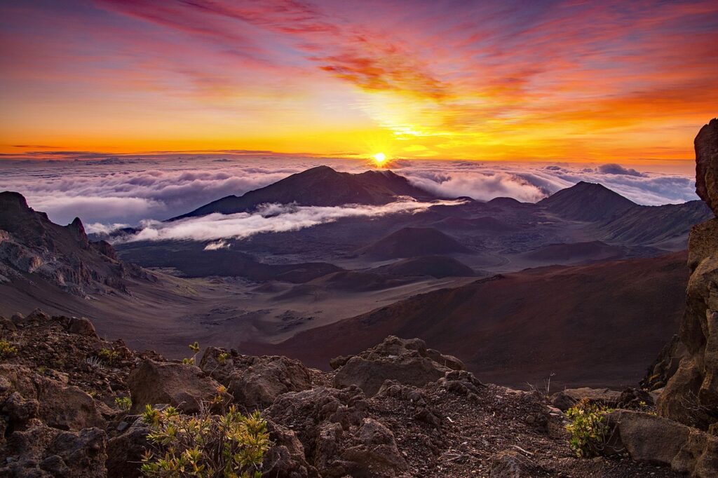 Sunrise over a volcanic landscape with rocky foreground and a sea of clouds at dawn behind dark volcanic cones.